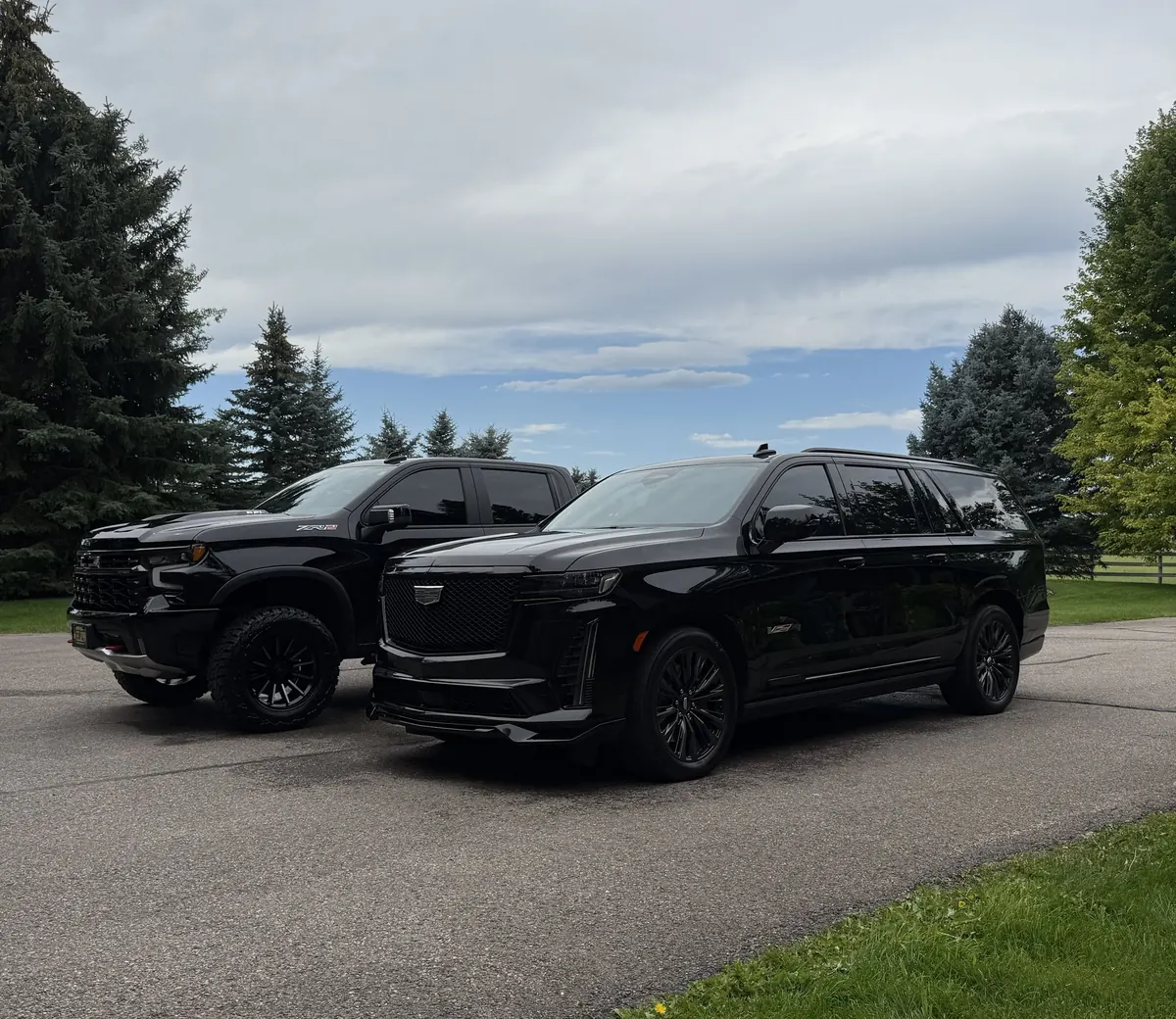 Black Cadillac Escalade and black Chevrolet truck on a driveway after maintenance details